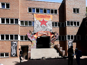 Eingang zum ehemaligen Hallenbad Ost ist mit enem Banner der Künstler Taring Padi geschmückt, davor Besucher der d15i